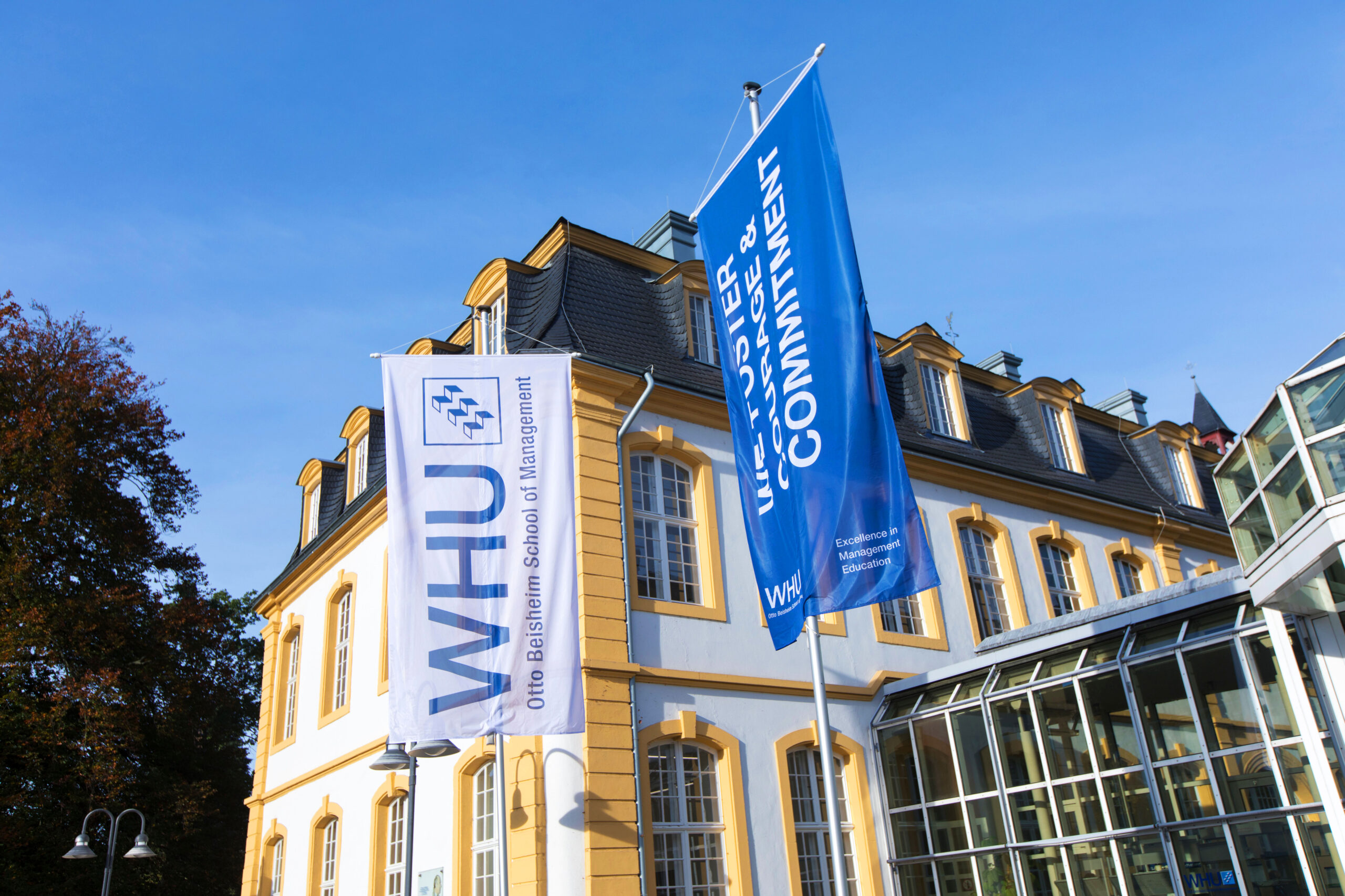 WHU campus building with WHU flags displayed in front of the entrance on a sunny day.